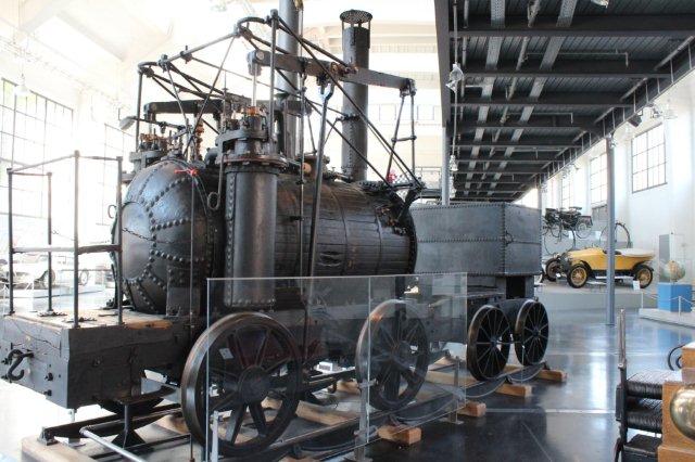 Trafikmuseet i München havde også en kopi af verdens første brugbare lokomotiv, Puffing Billy fra 1814. Originalen står i London på South Kensington-Museet. Kopien her er bygget med en kedelbeklædning, hvor selv mørnede beklædningsbrædder er gengivet! William Hedleys lokomotiv kørte ved Wylam-kulminen 1814 - 1862. Det var på 25 hk, havde en vægt på 9,19 t uden tender og kunne køre 10 km/t. Kopien er bygget i Tyskland til museet i München i 1906. Foto fra 30.08.2013.